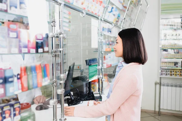 Side view of asian customer holding bottles with pills near seller in drugstore — Stock Photo