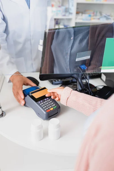 Vista recortada del cliente pagando con tarjeta de crédito en terminal de pago en farmacia - foto de stock