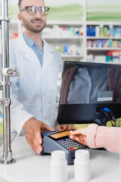 Cliente que paga con tarjeta de crédito en la terminal de pago cerca del vendedor en la farmacia - foto de stock