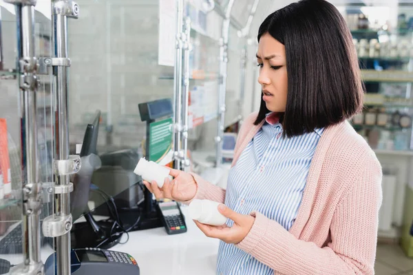 Mécontent asiatique femme tenant bouteilles avec pilules dans drugstore — Photo de stock
