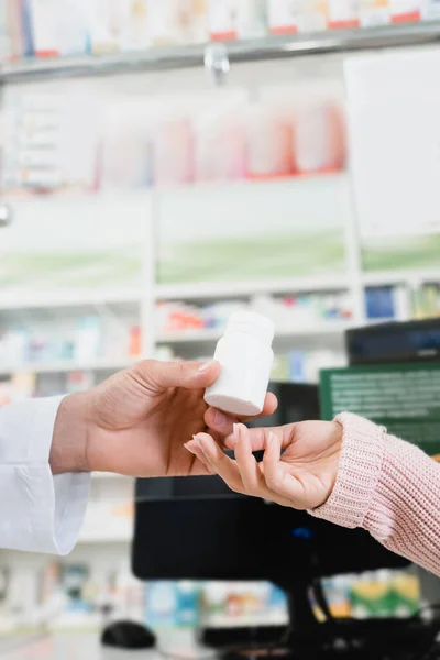 Vista ritagliata del farmacista dando bottiglia con pillole al cliente — Foto stock