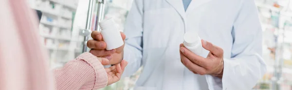 Vue recadrée du pharmacien donnant bouteille avec des pilules au client, bannière — Photo de stock