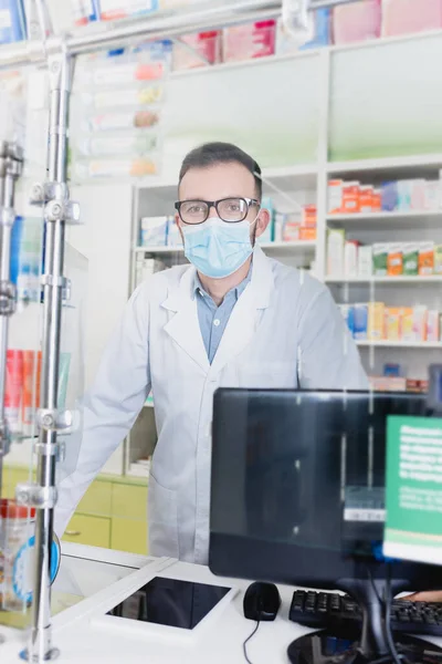 Farmacéutico en gafas y máscara médica mirando a la cámara en la farmacia - foto de stock