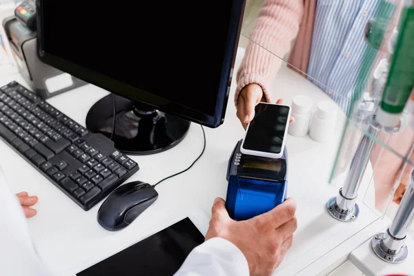 Vista recortada del cliente que paga con teléfono inteligente en la farmacia - foto de stock