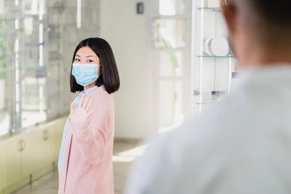 Asian woman in medical mask waving hand to pharmacist in drugstore — Stock Photo