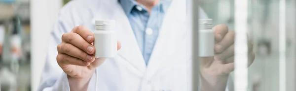 Ausgeschnittene Ansicht eines Apothekers, der eine Flasche mit Tabletten in Glasnähe hält, im unscharfen Vordergrund, Banner — Stockfoto