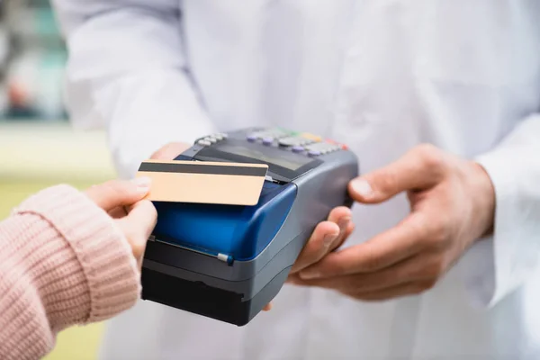 Partial view of pharmacist holding payment terminal while customer paying by credit card in drugstore — Stock Photo
