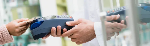 Ausgeschnittene Ansicht des Apothekers mit Zahlungsterminal, während der Kunde in der Drogerie mit Kreditkarte bezahlt, Banner — Stockfoto