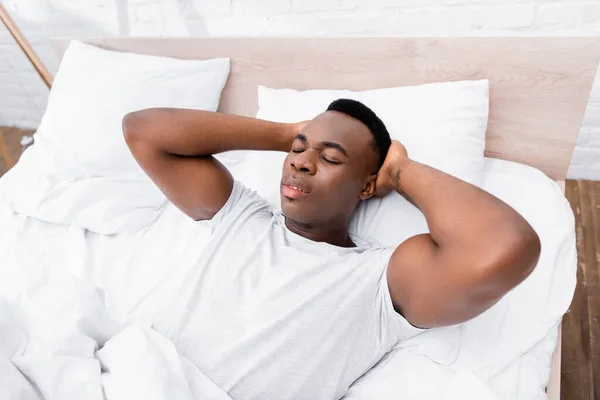 Africano americano com as mãos perto da cabeça deitada na cama de manhã — Fotografia de Stock