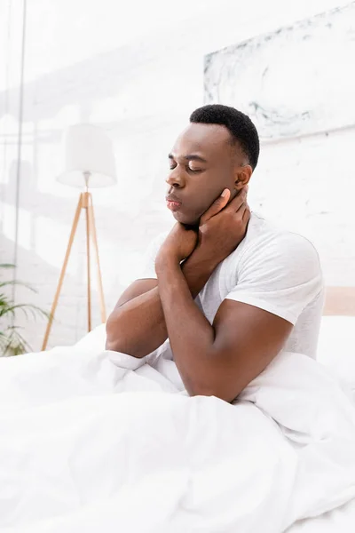 Hombre afroamericano sufriendo de dolor en el cuello en la cama - foto de stock
