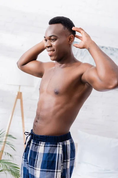 Shirtless african american man smiling while stretching at home during morning — Stock Photo