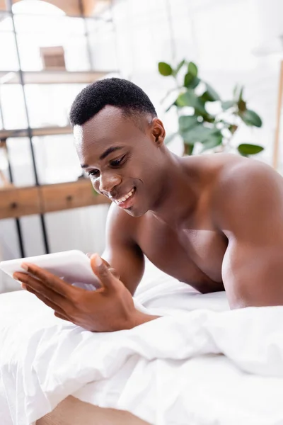 Shirtless african american man using digital tablet on bed at morning — Stock Photo