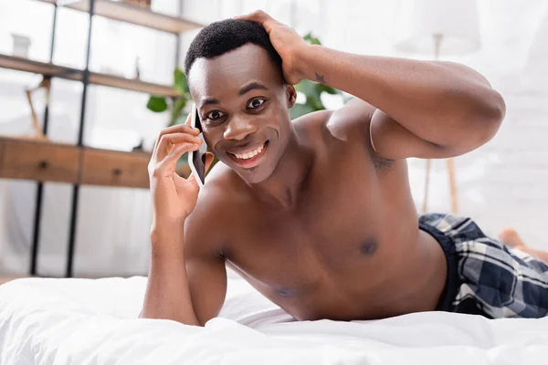 Sorrindo homem americano africano falando no smartphone na cama em casa — Fotografia de Stock