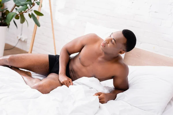 Musculoso afroamericano hombre en calzoncillos acostado en la cama - foto de stock