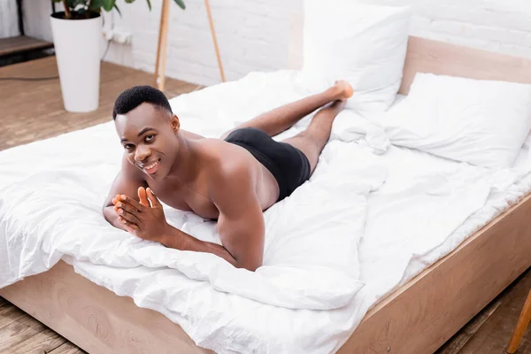 Sorrindo afro-americano homem de cuecas deitado na cama em casa — Fotografia de Stock