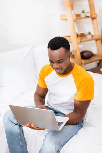 Joyeux freelance afro-américain utilisant un ordinateur portable sur le lit le matin — Photo de stock