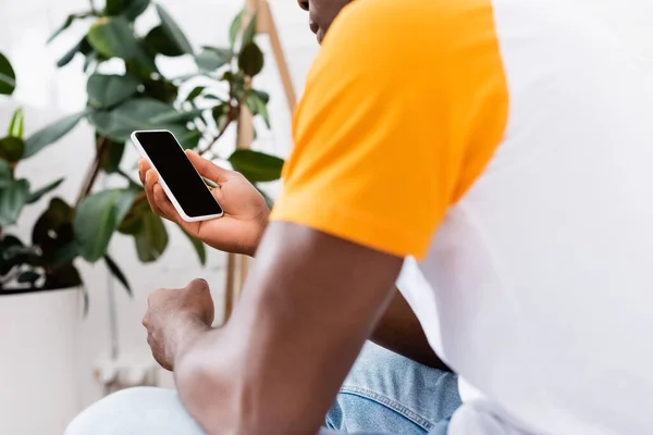 Ausgeschnittene Ansicht eines Afroamerikaners, der zu Hause ein Smartphone mit leerem Bildschirm hält — Stockfoto