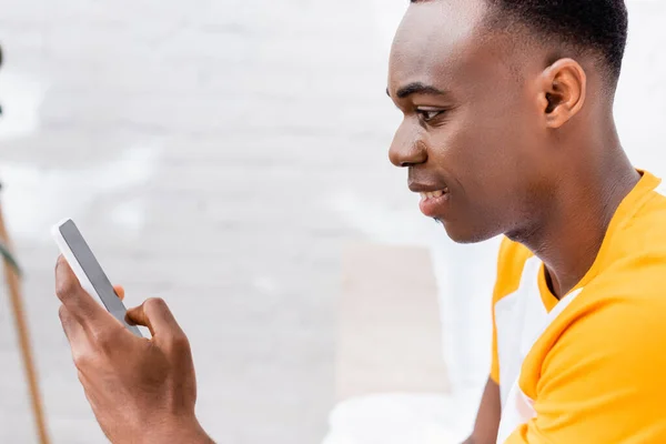 Sonriente hombre afroamericano usando teléfono inteligente con pantalla en blanco en casa - foto de stock