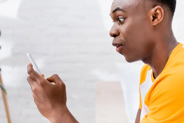 Homem americano africano chocado usando smartphone em casa — Fotografia de Stock