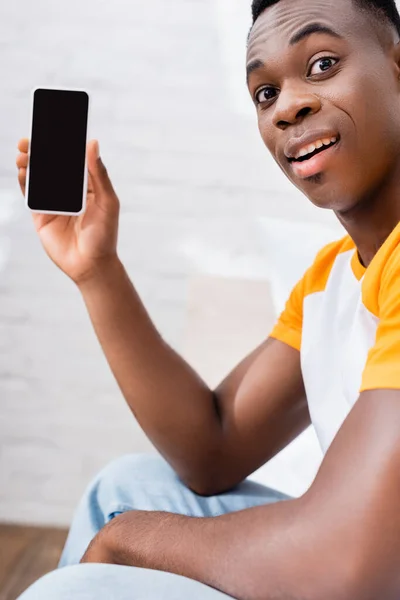 Homme afro-américain excité montrant smartphone avec écran blanc à la maison — Photo de stock