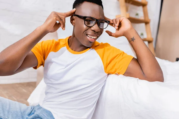 African american man in eyeglasses looking away near bed at home — Stock Photo