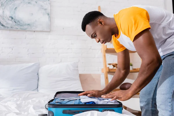 Uomo afroamericano che mette i vestiti in valigia sul letto a casa — Foto stock