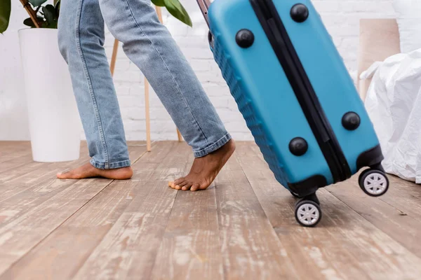 Обрізаний вид босоніж афроамериканця, що йде біля валізи вдома — стокове фото