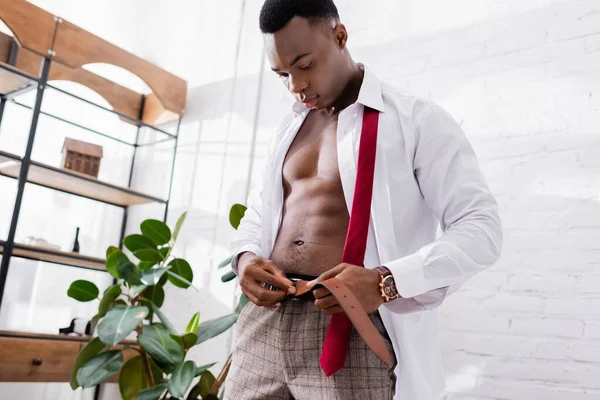Musculoso hombre de negocios afroamericano usando cinturón de cintura en casa - foto de stock