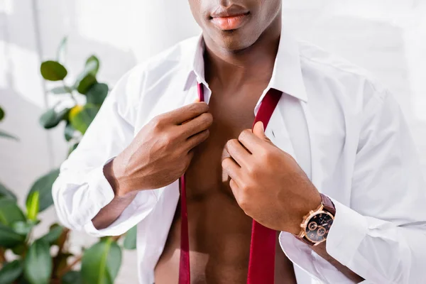 Розбитий погляд на афроамериканського бізнесмена, який тримає червону краватку, одягаючись вдома. — стокове фото