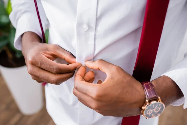 Cropped view of african american businessman buttoning shirt at home — Stock Photo