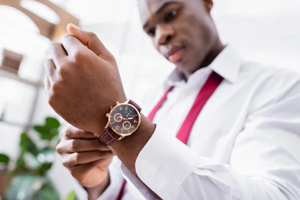 Reloj de pulsera a mano del empresario afroamericano sobre fondo borroso en casa - foto de stock