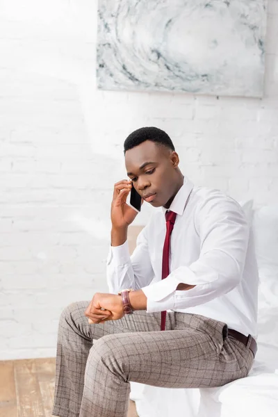 Afrikanischer Geschäftsmann checkt Zeit, während er auf dem Smartphone im Bett spricht — Stockfoto