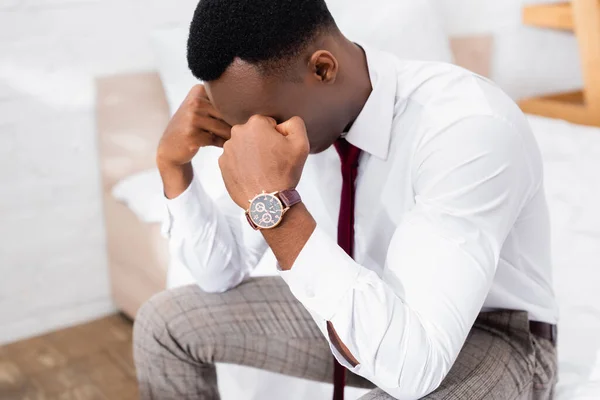 Расстроенный африканский американский бизнесмен сидит на кровати на размытом фоне — стоковое фото