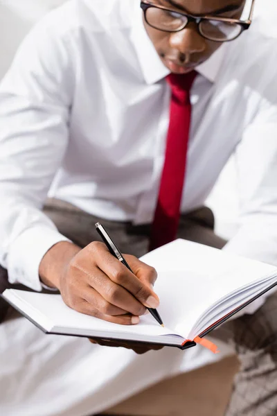 Stylo et cahier entre les mains d'un homme d'affaires afro-américain sur fond flou — Photo de stock