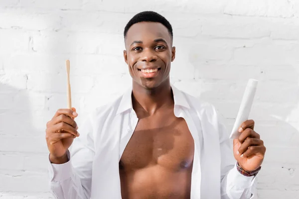 Allegro uomo africano americano che tiene dentifricio e spazzolino da denti a casa — Foto stock
