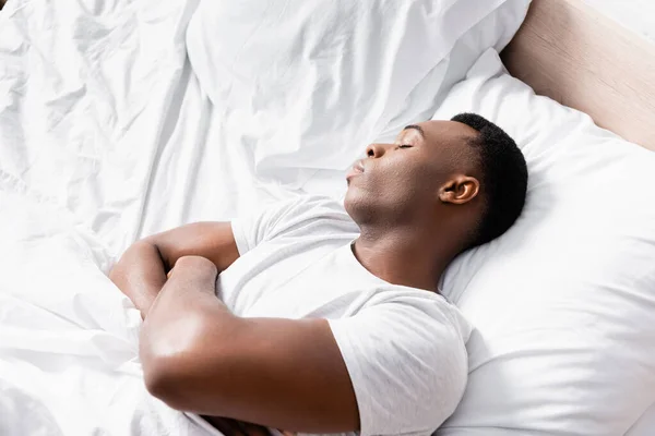 Vue en angle élevé de l'homme afro-américain avec les bras croisés dormant sur le lit le matin — Photo de stock