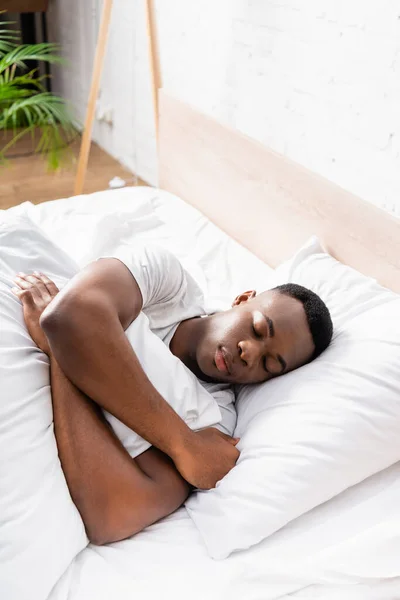 Afro americano uomo abbracciare coperta mentre dormire su letto a casa — Foto stock