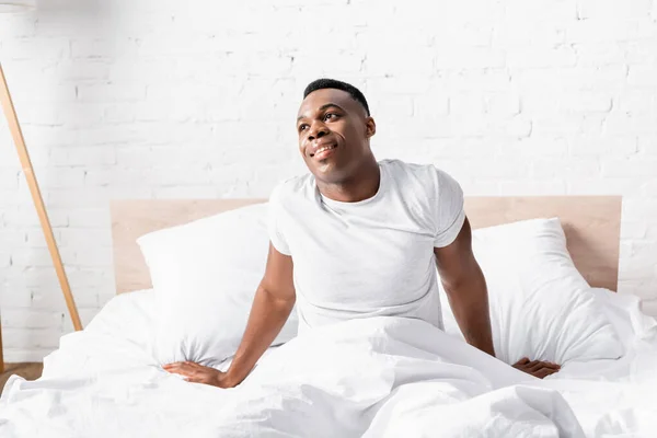 Sonriente hombre afroamericano sentado en la cama por la mañana - foto de stock