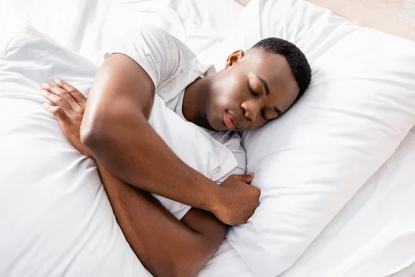 Vista ad alto angolo dell'uomo afroamericano che abbraccia il cuscino mentre dorme a casa — Foto stock