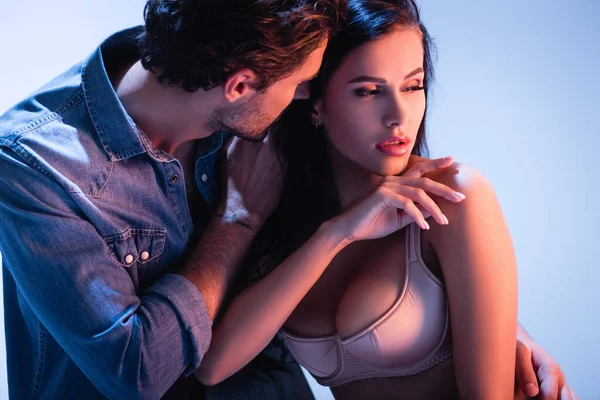 Uomo in denim camicia abbracciando ragazza sexy in reggiseno di raso su sfondo blu — Foto stock