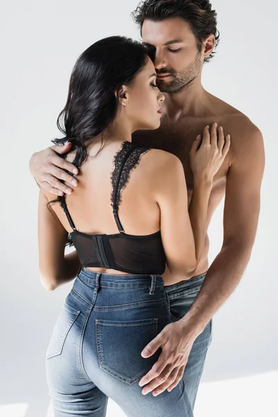 Спокуслива жінка в бюстгальтері і джинсах, торкаючись грудей м'язового хлопця на сірому фоні — стокове фото