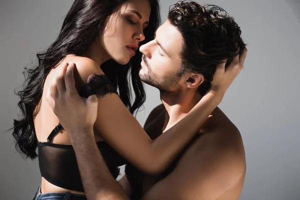 Sexy Frau im BH küsst und berührt die Haare ihres hemdslosen Freundes auf grauem Hintergrund — Stockfoto