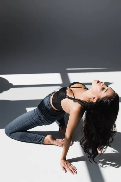 Sexy mulher descalça no sutiã e jeans no fundo cinza com sombra — Fotografia de Stock