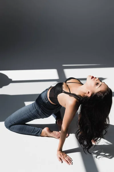 Sexy mujer descalza en sujetador y jeans sobre fondo gris con sombra - foto de stock