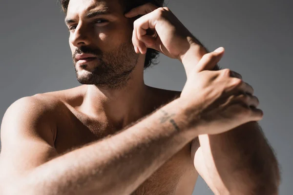 Uomo senza maglietta con mano vicino alla testa guardando la fotocamera isolata sul grigio — Foto stock