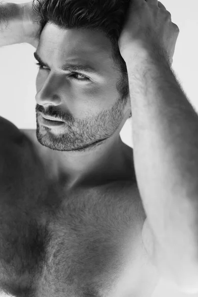 Tiro monocromático de homem sem camisa barbudo com a mão perto da cabeça olhando para longe isolado em cinza — Fotografia de Stock