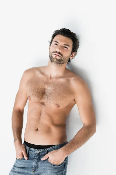 Junger Mann ohne Hemd mit Händen in Jeanstaschen und Blick in die Kamera auf weißem Hintergrund — Stockfoto