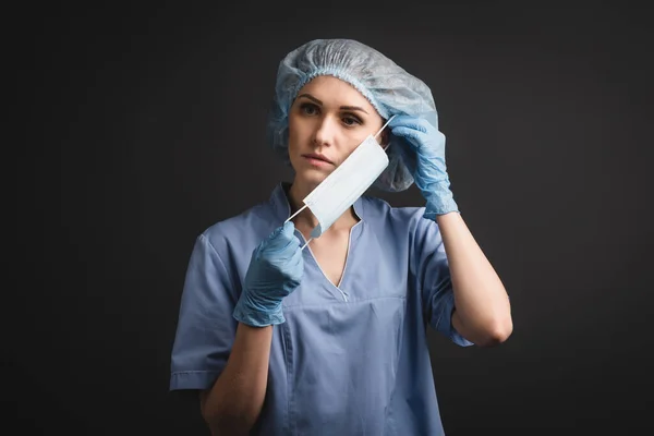 Enfermeira em tampa médica usando máscara isolada em cinza escuro — Fotografia de Stock