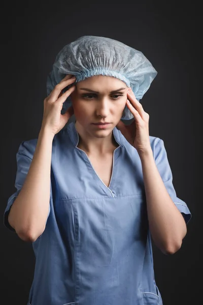 Enfermeira cansada em tampa médica que sofre de enxaqueca isolada em cinza escuro — Fotografia de Stock