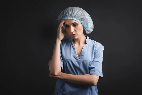 Infirmière en bonnet médical bleu ayant mal à la tête isolé sur gris foncé — Photo de stock